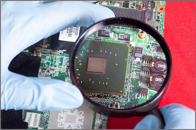 Magnifier in hands with blue gloves showing or looks on printed circuit board.jpg