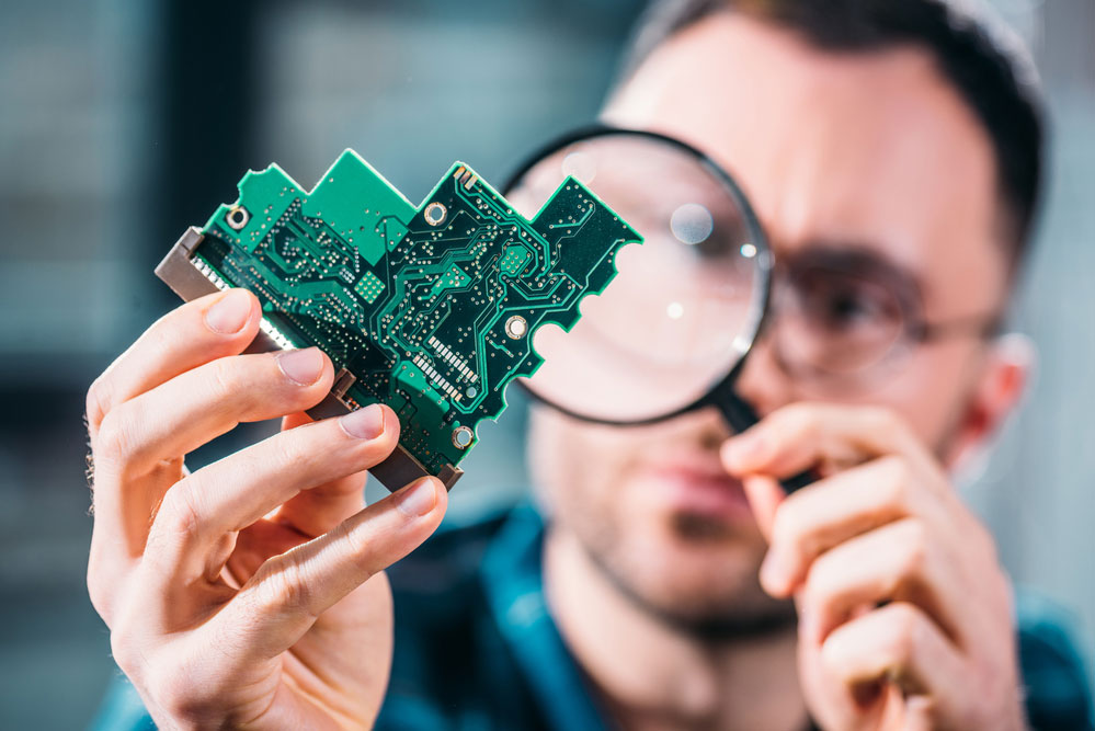 4 Layer PCB:Close-up view of man looking at circuit board through a magnifying glass